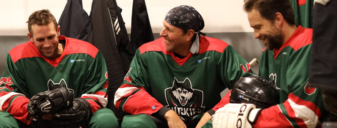 Hockey players in red and black jerseys with sponsor logos on the ice during a game.