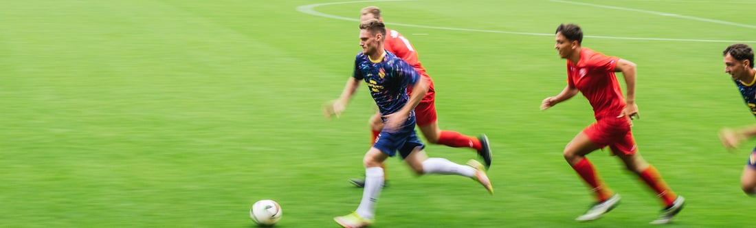 Fußballspieler in selbstgestalteten Trikots verfolgen den Ball auf dem Spielfeld.