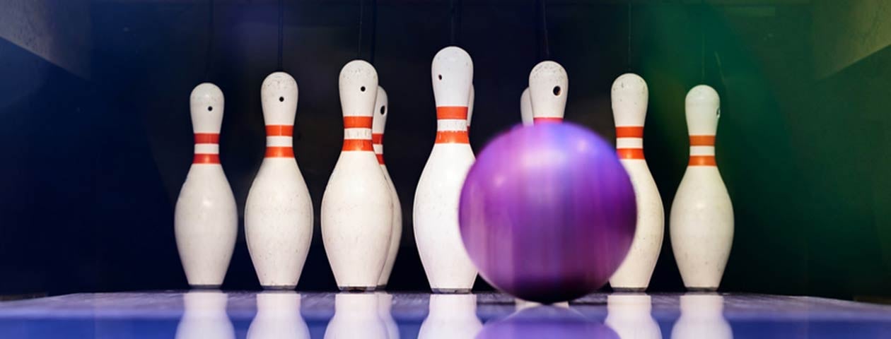 The image shows a bowling alley with pins and a bowling ball lying on the floor. The pins are white with red stripes.