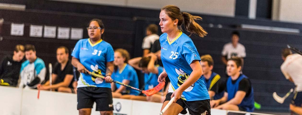 Un groupe de joueurs de floorball portant des maillots personnalisés de la marque 'owayo'. Les joueurs sont vus dans un stade intérieur en train de jouer au jeu.