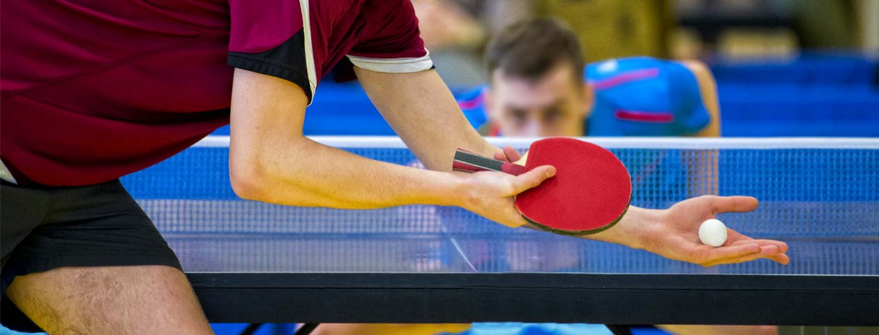 Un homme joue au tennis de table et tient une raquette de ping-pong en main tout en se préparant à servir la balle.