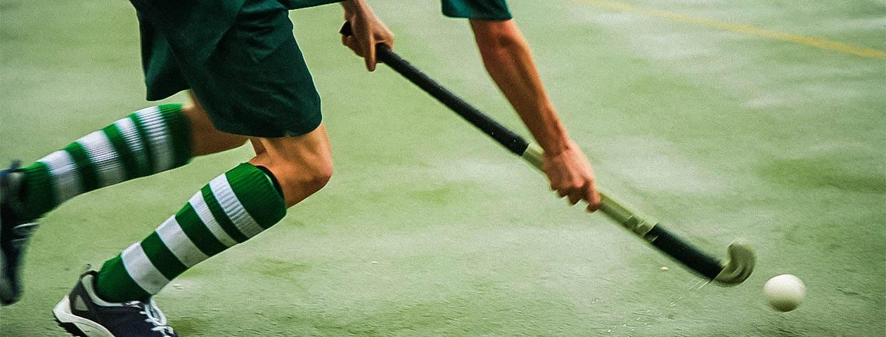 A field hockey player is shown wearing a self-designed jersey with green and white stripes, along with matching socks, while holding a hockey stick.