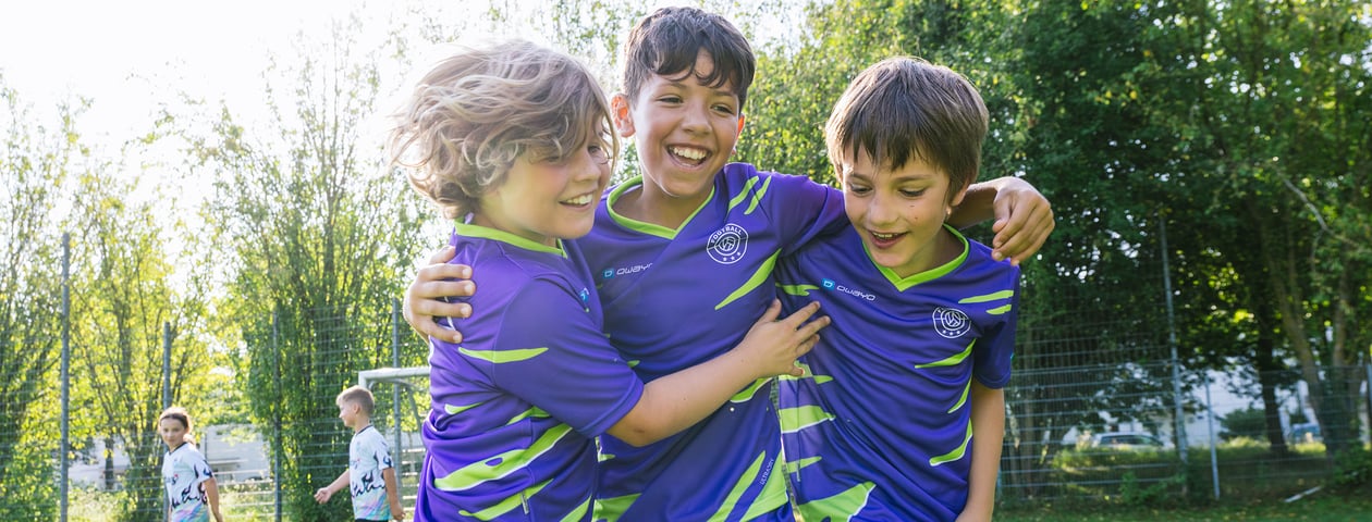 Three children in customized soccer jersey hug each other laughing