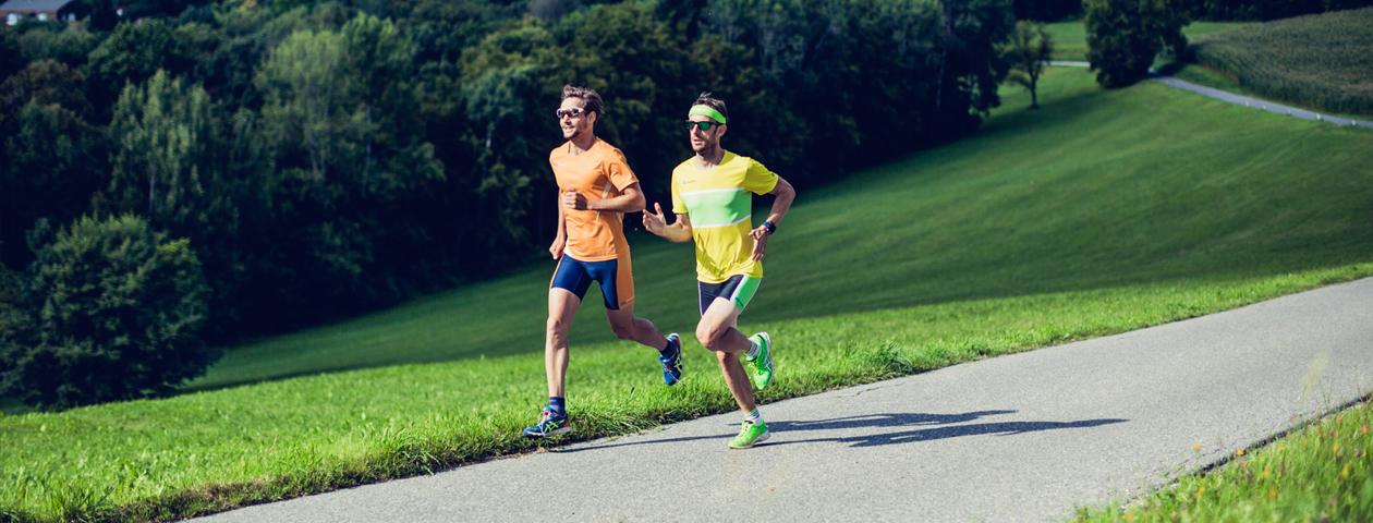 Twee hardlopers in kleurrijke hardloopshirts lopen over een bosweg.