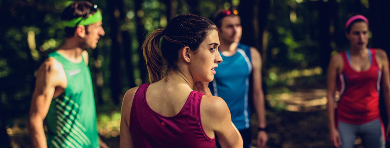 Een groep mensen met hardloop tanktops staat in het bos en lijkt zich voor te bereiden op een sportieve activiteit.