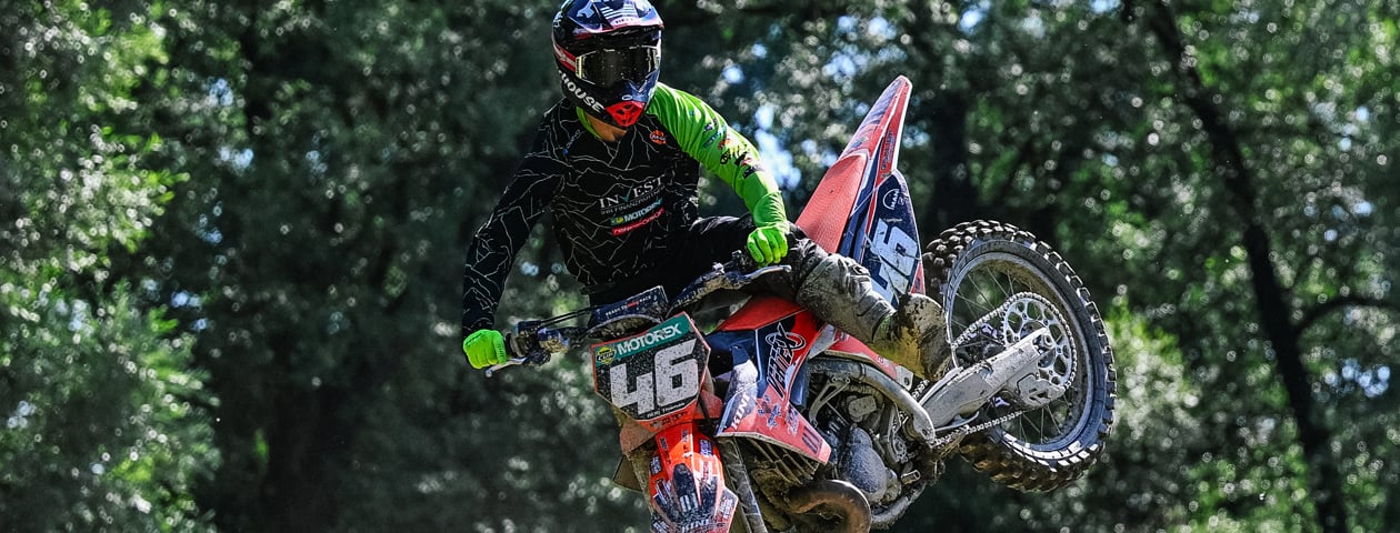 Ein Motocross-Fahrer trägt ein selbstgestaltetes Trikot von 'owayo' und fährt auf einem Motorrad durch einen Wald.