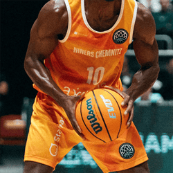 Klicken Sie hier, um unsere Basketballprodukte zu sehen Ein Basketballspieler in einem orangefarbenen Trikot mit der Aufschrift 'NINERS CHEMNITZ' und der Nummer 10. Er hält einen orangefarbenen Basketball von Wilson.