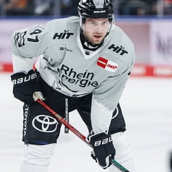 Klicken Sie hier, um unsere Eishockeyprodukte zu sehen Ein Eishockeyspieler trägt ein Trikot mit der Aufschrift 'Rheinenergie' und anderen Sponsorenlogos. Er hält einen Eishockeystab in der Hand.