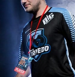 Click here to see our esports products A man is wearing a black jersey with the text 'TRIPEDO' and a logo that suggests it belongs to a sports brand. He has a red name tag around his neck with the word 'PLAYER' on it.