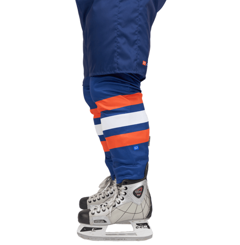 Side view of an ice hockey player wearing blue pants with orange and white stripes, and a CCM ice hockey skate.