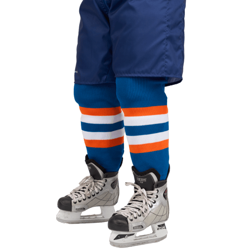Ein Model zeigt eine Eishockeysocke mit blauen, orangefarbenen und weißen Streifen, die über einer blauen Hose und Eishockeyschuhen getragen wird.