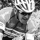 A cyclist wearing a helmet and a jersey with the text 'MALVIBER' and 'graffiti' on it. The background is blurred.