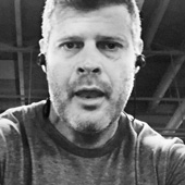 A man with a beard and short hair taking a selfie. He is wearing a jacket.