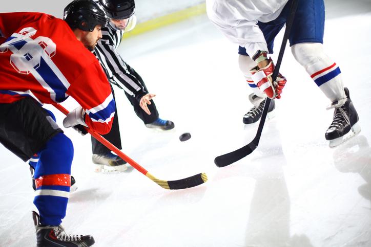 Ein Eishockeyspieler in einem roten Trikot mit der Nummer 88 und ein Schiedsrichter in schwarz-weißem Trikot kämpfen um den Puck auf dem Eis.