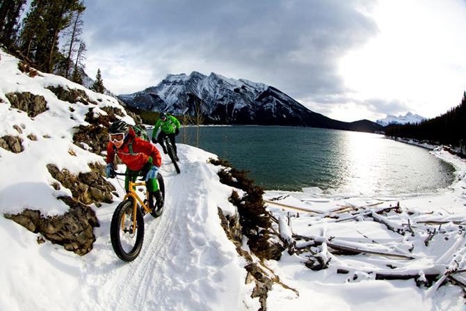 Cyclists riding fat bikes in the snow alongside a lake