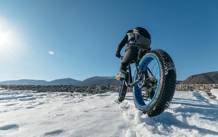 Gros plan d’un pneu fatbike, le fatbike et son sportif dans la neige