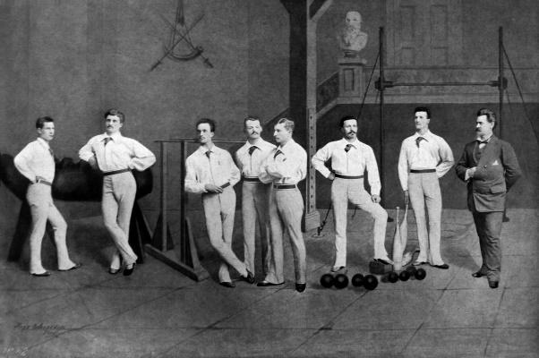 A black and white photo of athletes wearing button down shirts and long pants in a sports hall
