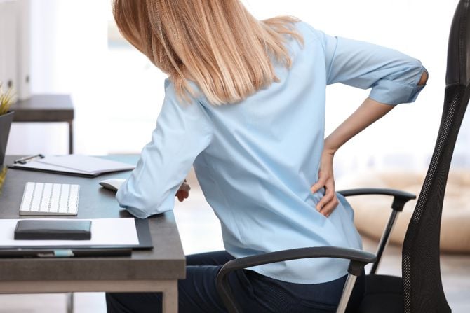 Frau mit Rückenschmerzen am Schreibtisch