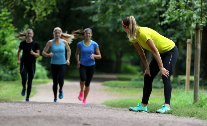 4 Läuferinnen auf einem Weg im Park, eine davon ruht sich aus, die anderen laufen.