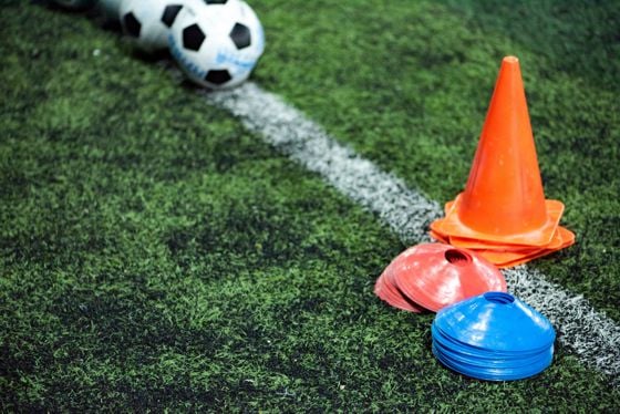Auf dem Kunstrasen liegen farbige Trainingsmarkierungen in rot, blau und orange neben einem Fußball.