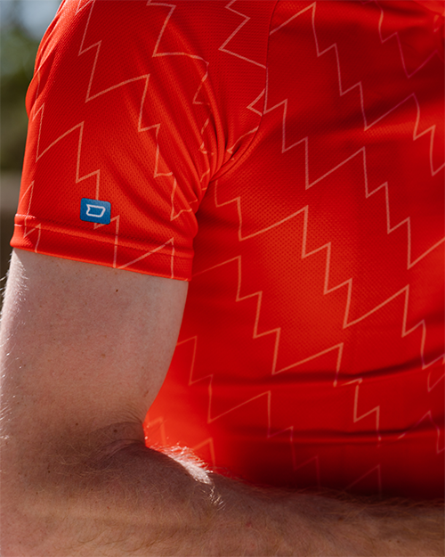 Un t-shirt de sport rouge avec un motif d'éclairs et une marque bleue sur l'épaule.