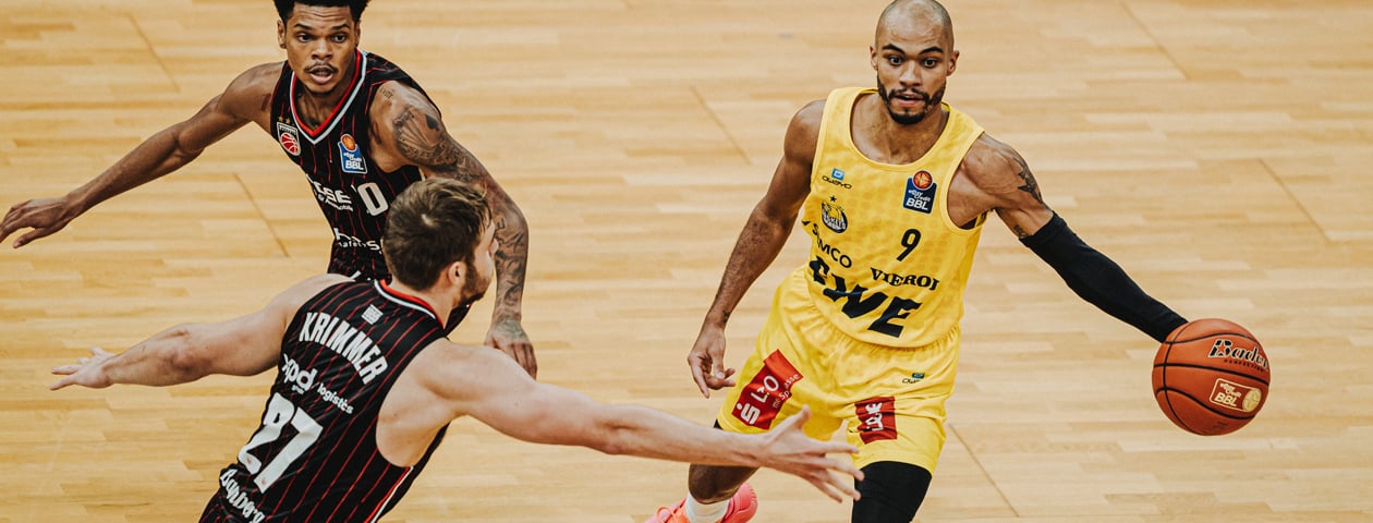 A basketball player in a red Owayo jersey during a game, holding a basketball while being defended by an opponent.