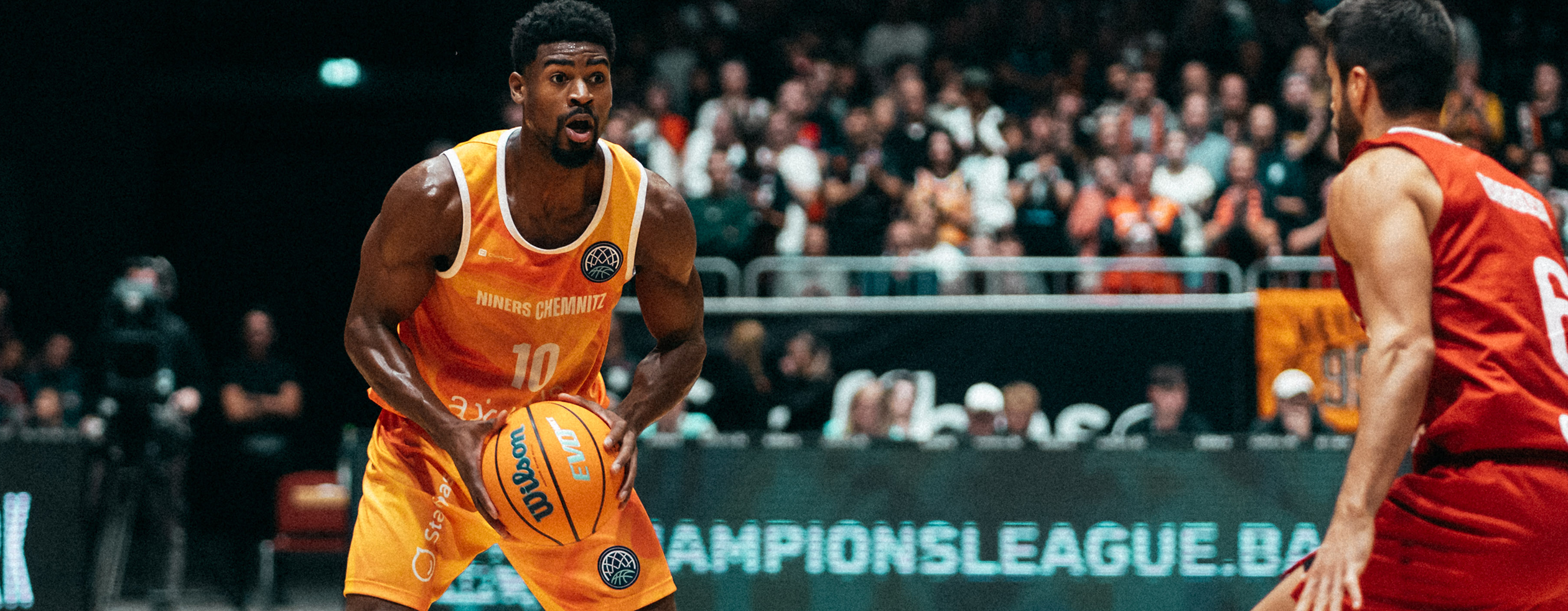 A basketball player in a yellow Owayo jersey dribbling while an opponent in a black jersey tries to defend him