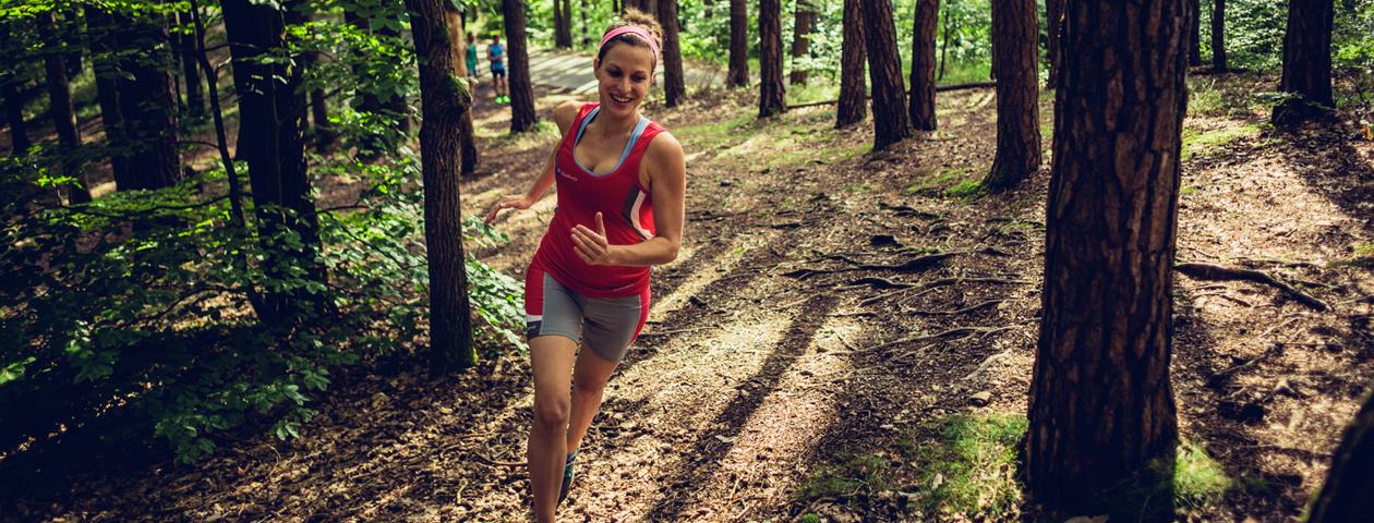 Coureuse à pied équipée d'un maillot personnalisé rouge flashy en train de courir dans les bois