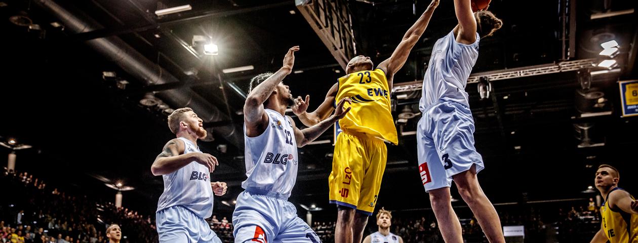 Basketballspeler in zelf ontworpen blauw basketballshirt die in de lucht springt met aanvallers in gele basketballteunues